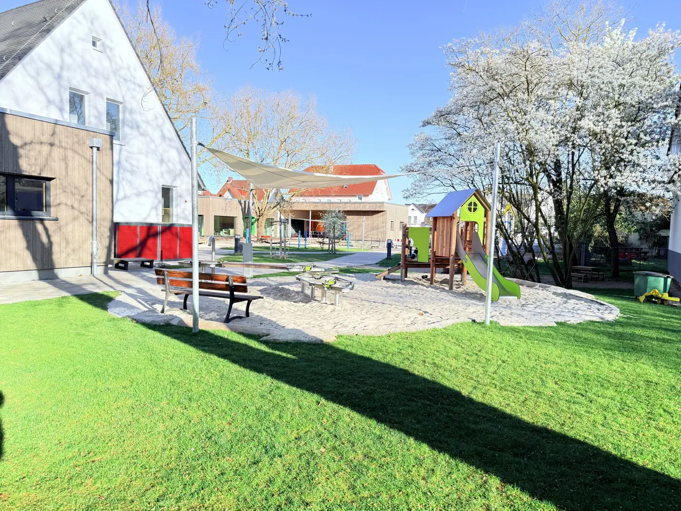 Sandspielbereich mit Bank und Spielhaus vor dem Gebäude im Frühling